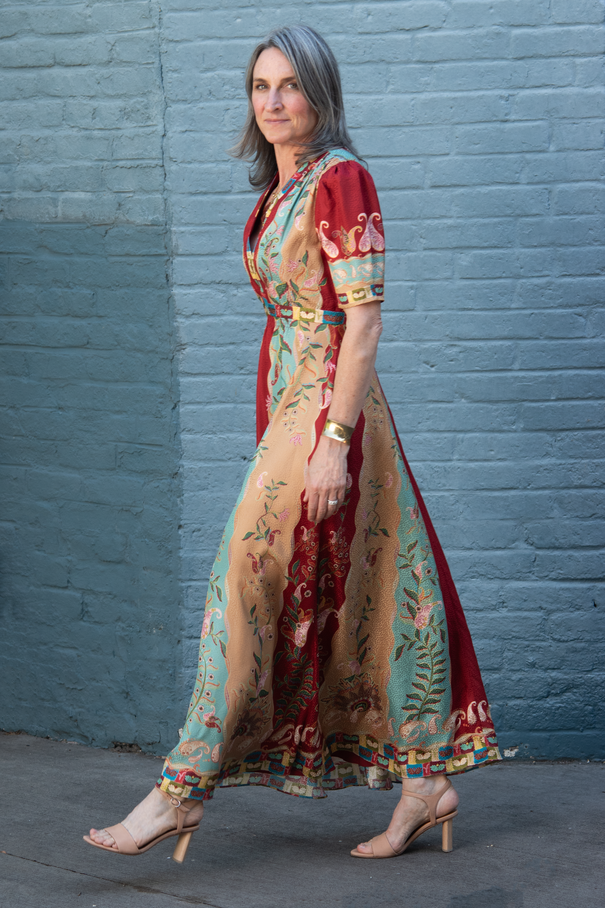 The satin, multicolor, mid-sleeve Saloni Tabitha dress on a model for scale. Dress features beautifully ornate natural motif pattern in red, aqua, and beige silk. 